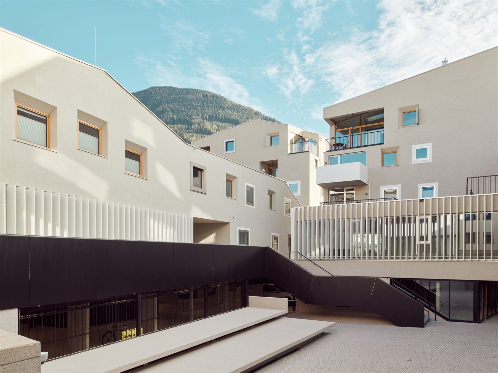 Quartier Raiffeisenplatz Schwaz — heller Wohnbau mit Balkonen und weissen Lamellen vor blauem Himmel